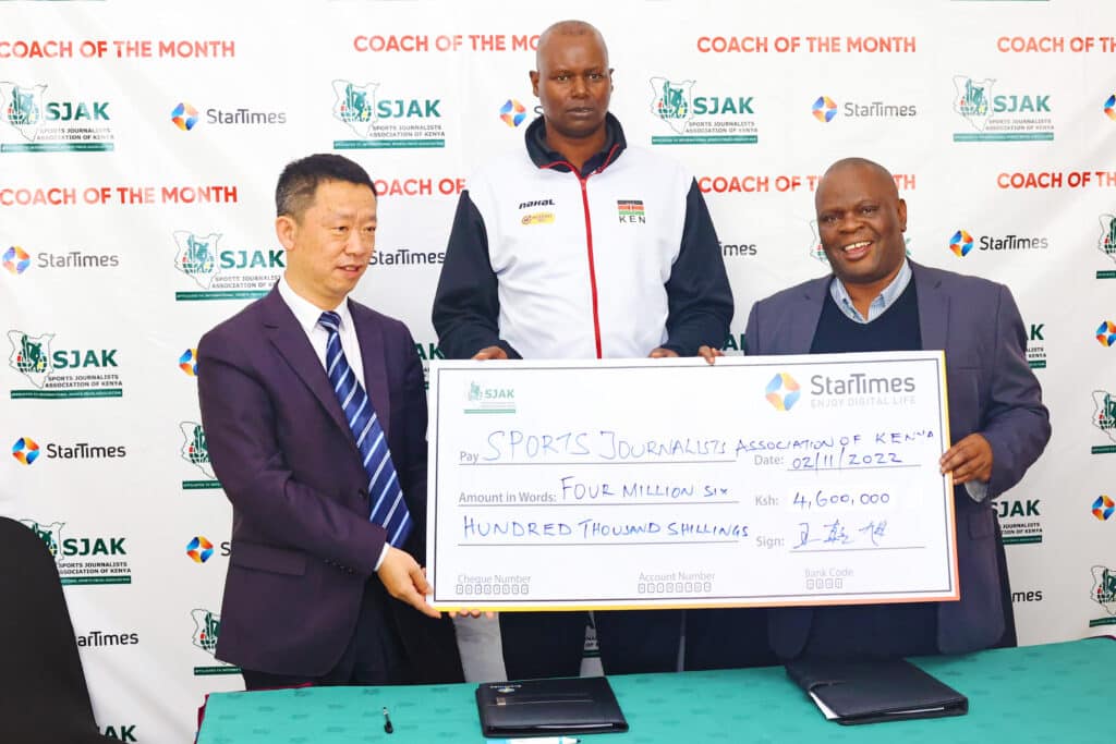 Startimes Kenya MD Andy Wang  (L) presents a cheque to SJAK president (R) Chris Mbaisi as the national volleyball women's team Malkia Strikers coach Paul Bitok looks on during the launch SJAK coach of the month sponsored by Startimes Kenya at a Nairobi hotel on November 2, 2022. Photo/ SJAK
