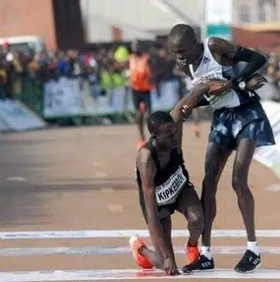 Simon Cheprot stops to help a runner during the Okpekpe Road Race